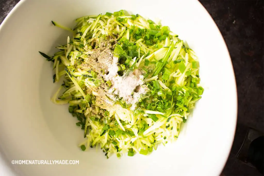 Zucchini thin julienne slices in a mixing bowl with seasoning for Zucchini Fritters Chinese Style