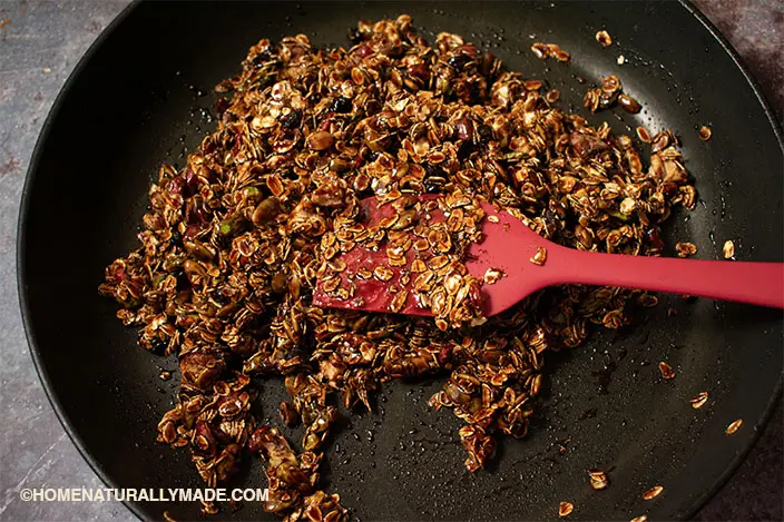 mix roasted rolled oats, nuts, seeds with burnt sugar in the hard anodized frying pan for homemade granola bars